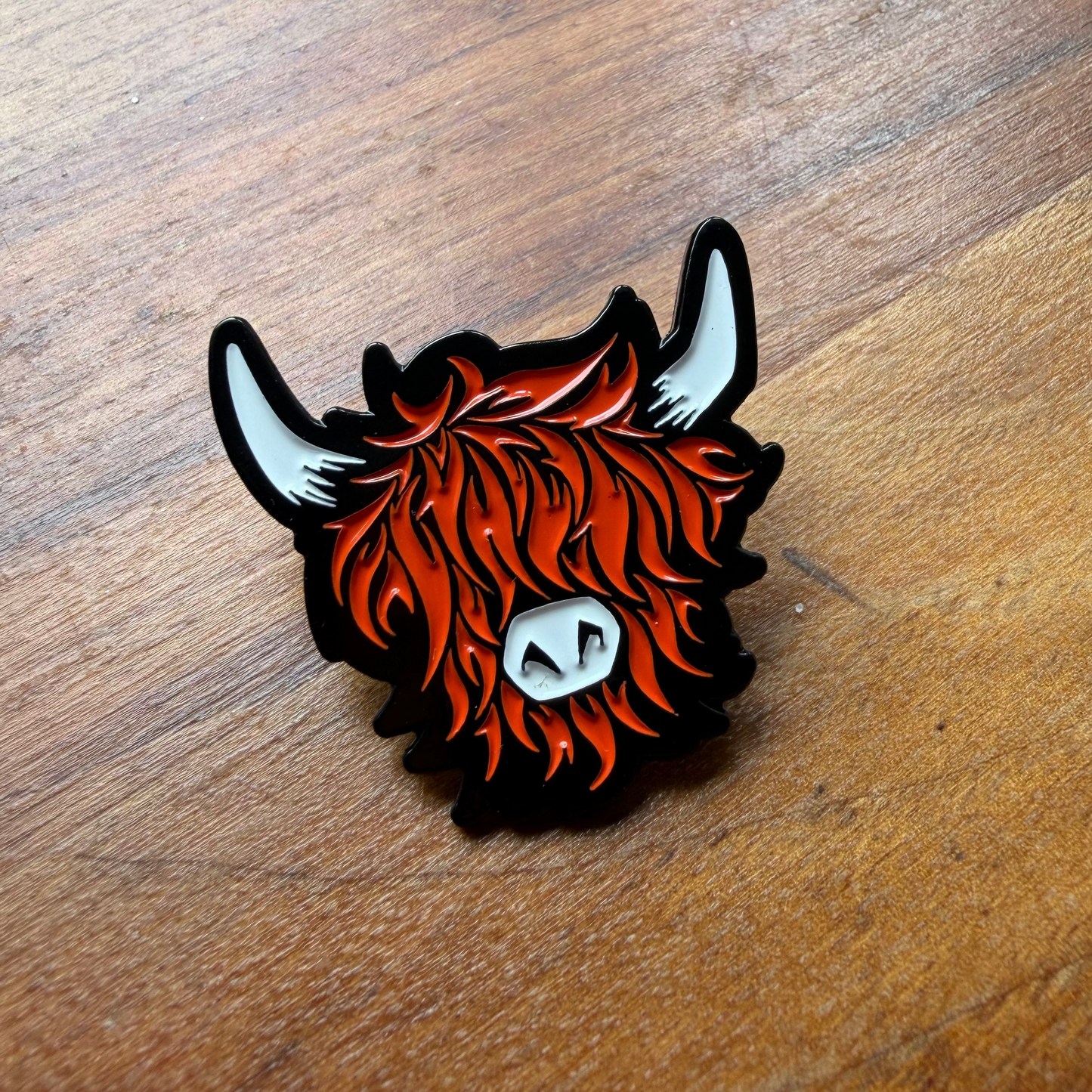 Enamel pin of a highland cow head on a wooden surface
